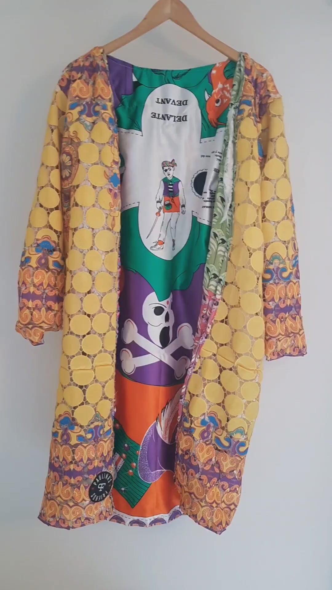 Close-up view of a vibrant, intricately designed fabric detail from an upcycled vintage kimono-style coat. Features bold yellow lace patterns, colorful floral embroidery, and a mix of rich, festive prints inspired by Canarian carnival aesthetics. A striking combination of textures and colors for a unique, eye-catching garment.